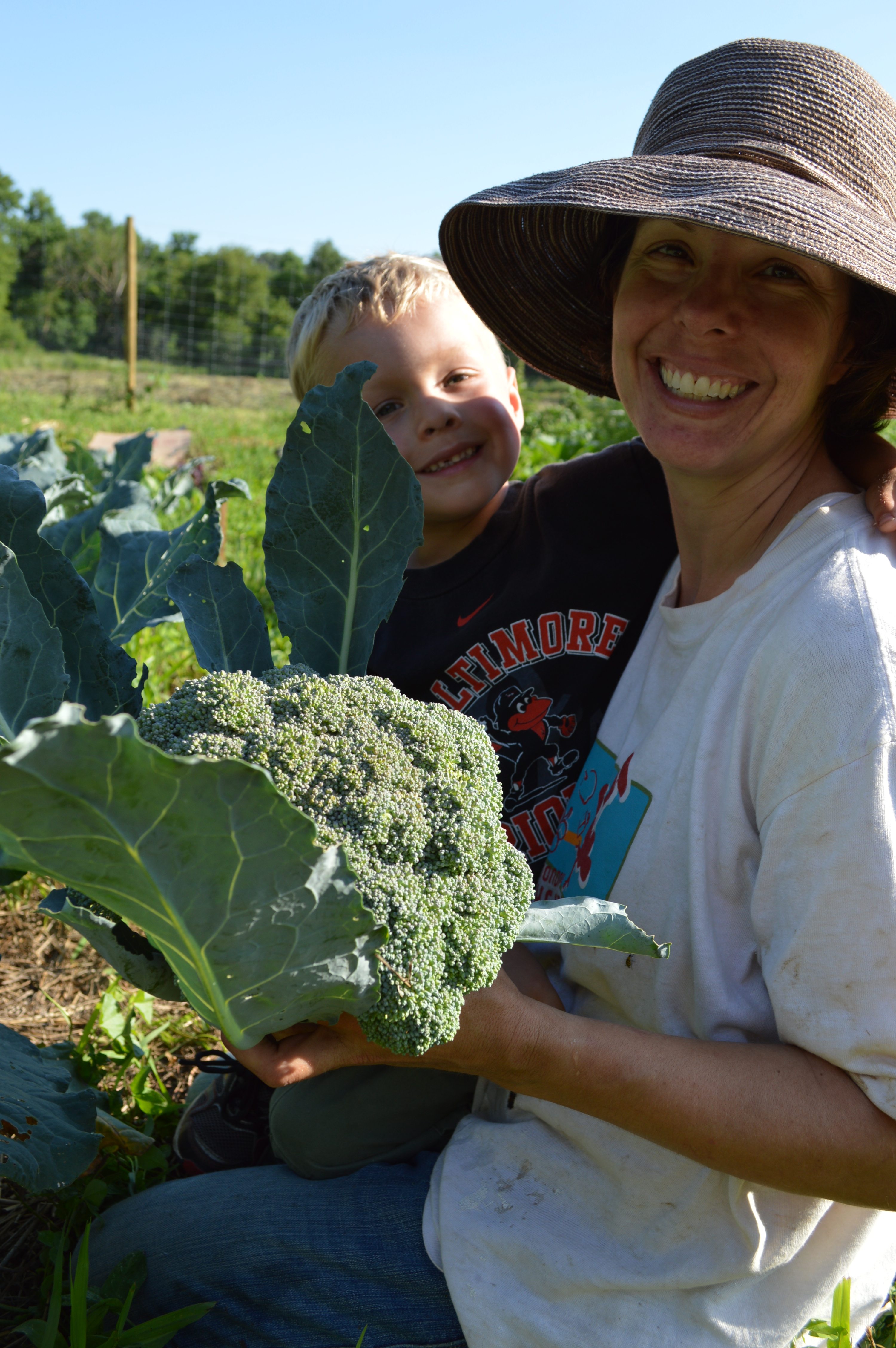 Female farmer and child sitting in farm field with harvested head of broccoli