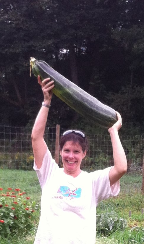 Woman holding up a giant zucchini.